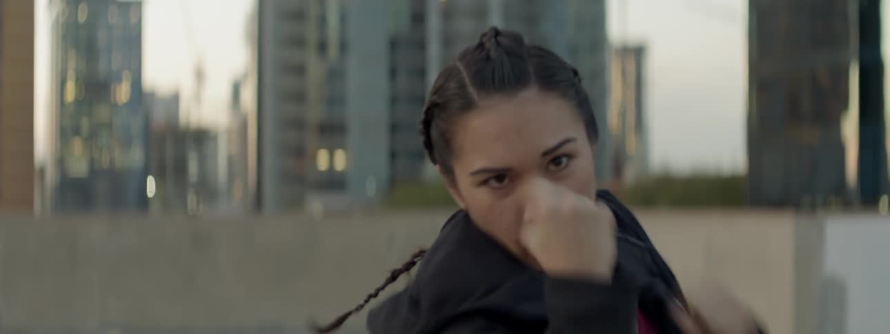 A woman punches the air on a city rooftop