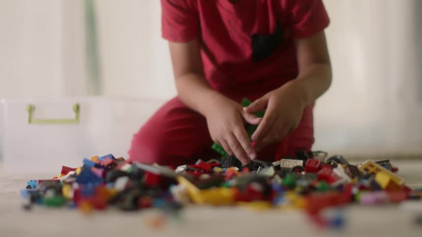 A boy is playing with building block bricks on the floor in a room in daylight