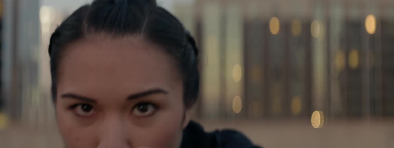 A female athlete is shadow boxing on a rooftop in a city at dusk