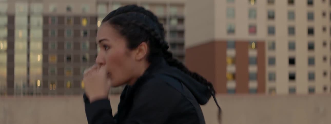 A female athlete is shadow boxing on a rooftop in a city at dusk