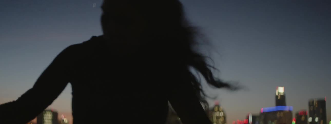 Woman exercising on a rooftop in a large city at sunset