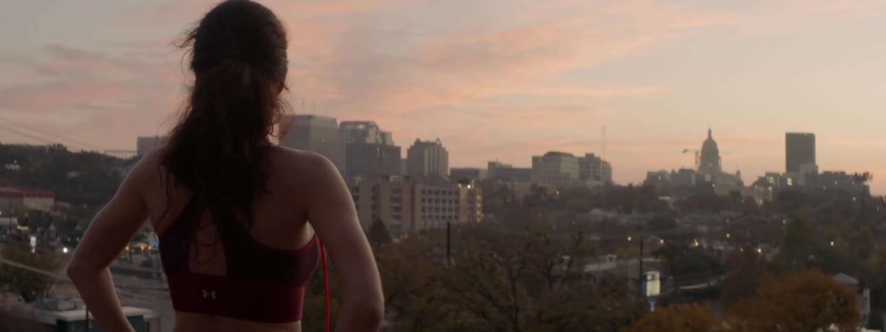 A female athlete is staring across a city at dusk