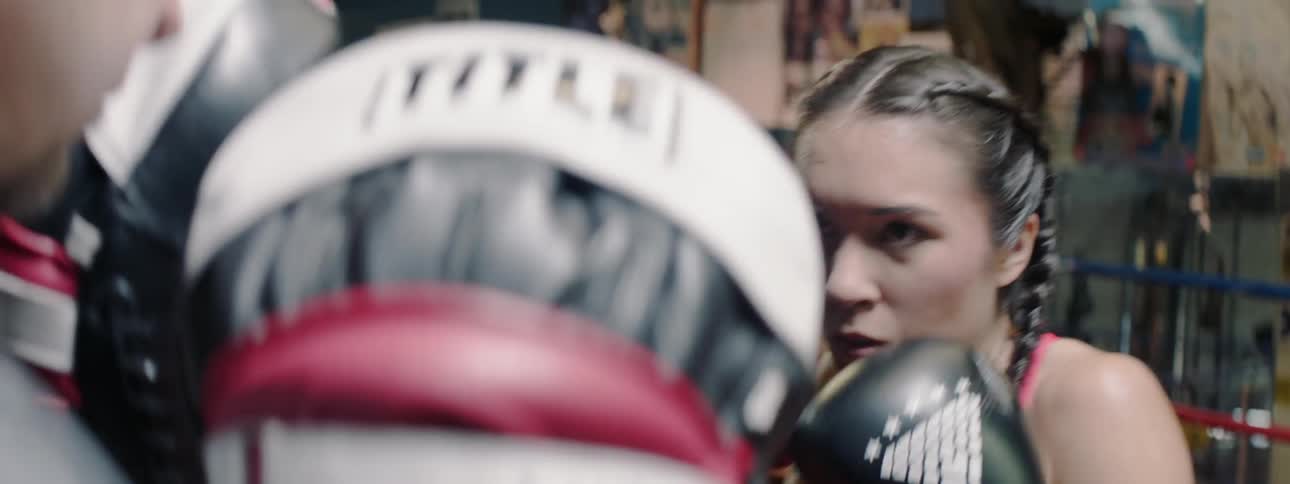 Woman wearing boxing gloves strikes another person wearing boxing gloves