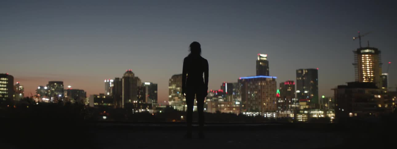 A woman is standing and looking out across a city at dusk