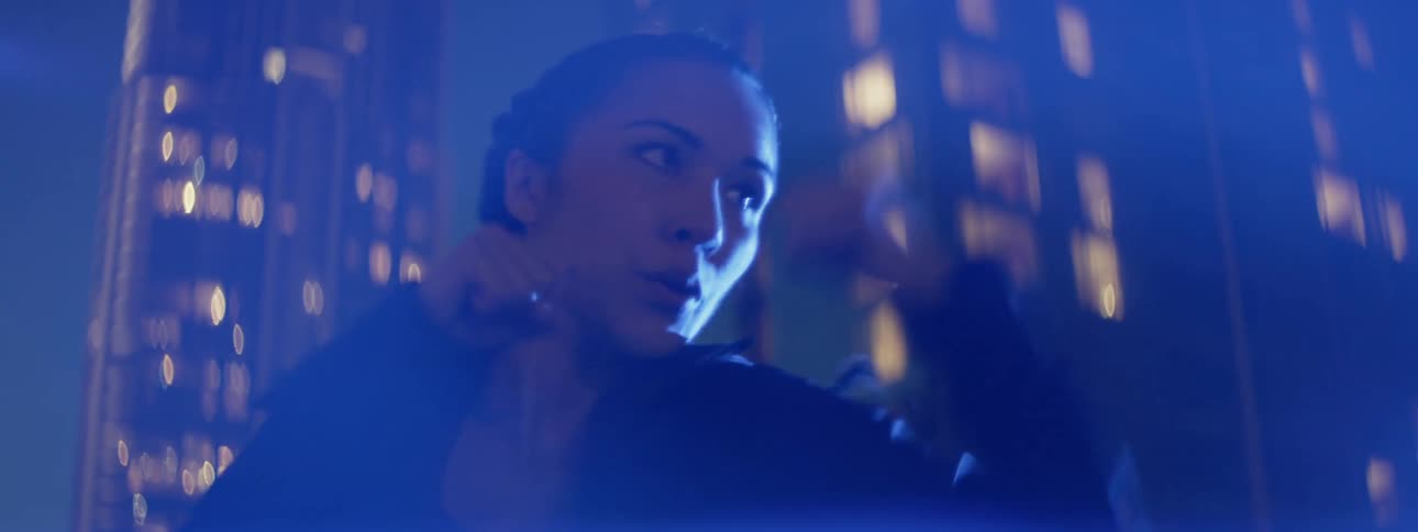 A female athlete is shadow boxing on a rooftop in a city at night