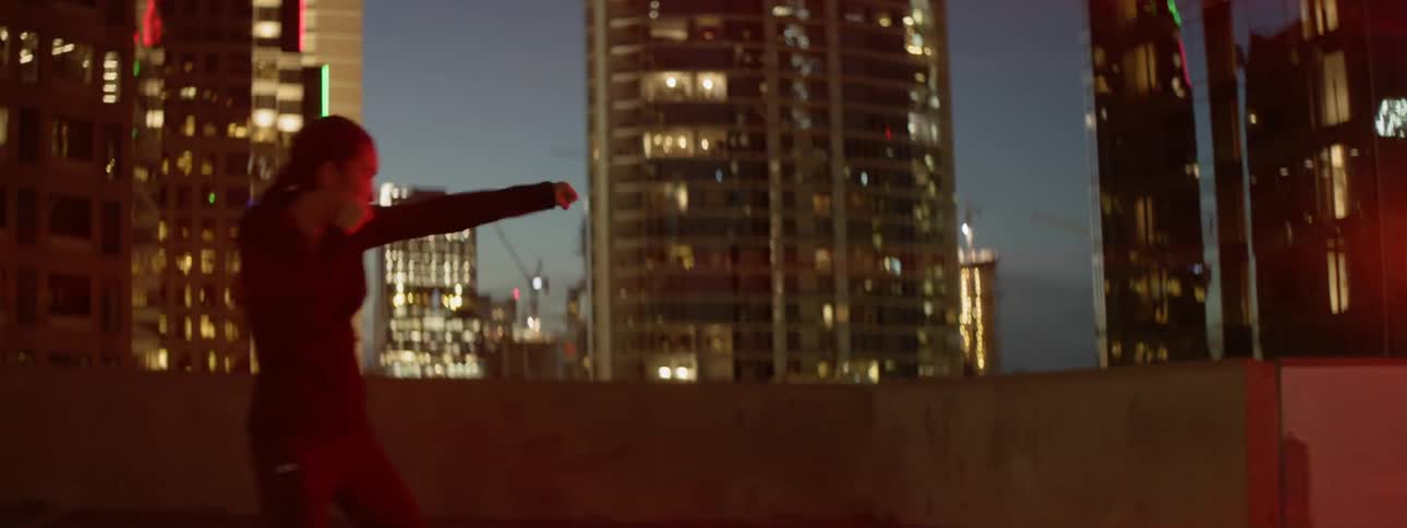 A woman shadow boxes atop a city building