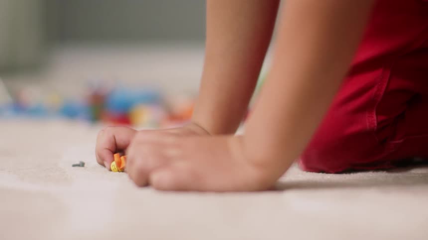A child is playing with building block characters and bricks on the ground in a room in daylight
