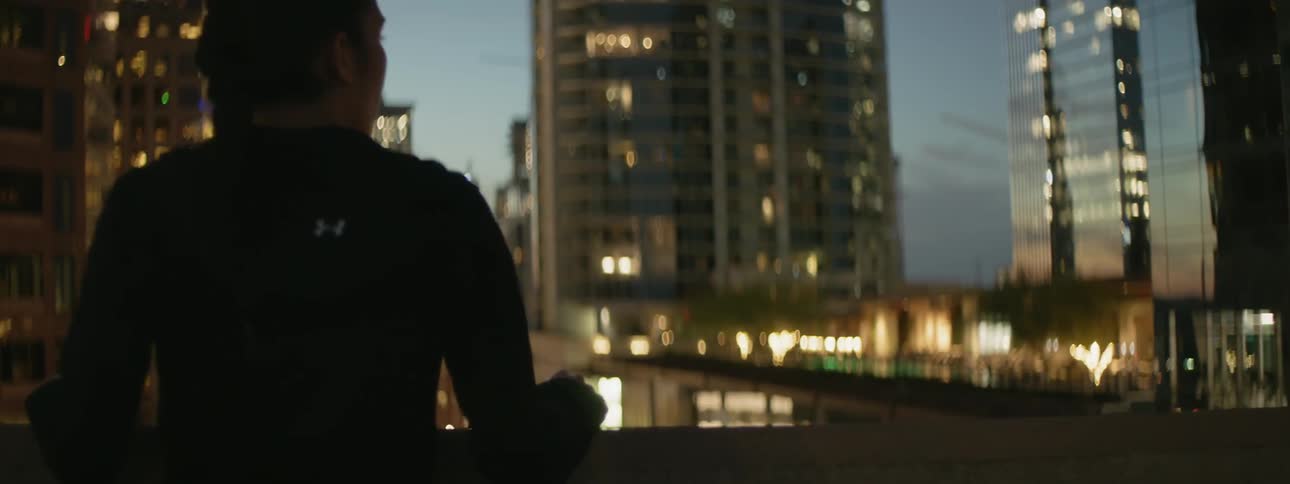 A woman stands on a city rooftop at dusk