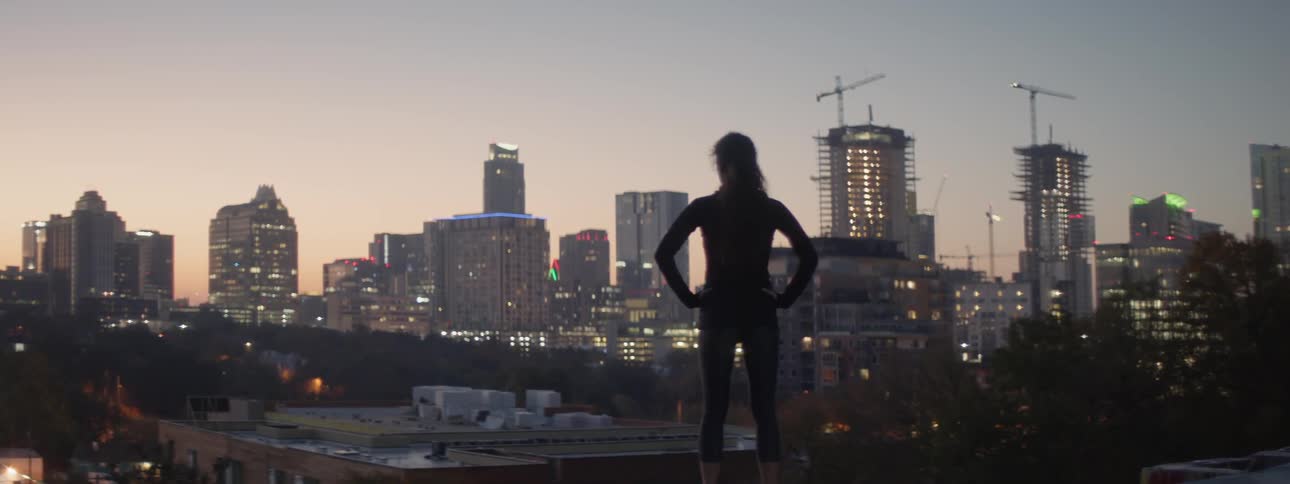 A woman stands on the roof looking over the city at dawn