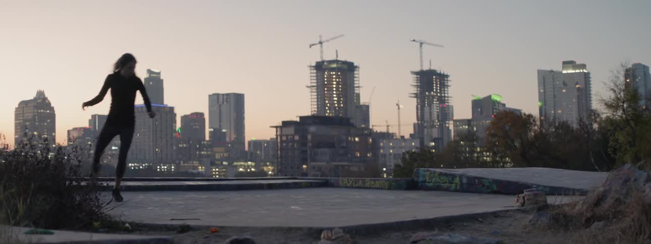 A female athlete is training on a rooftop on the outskirts of a city at dusk