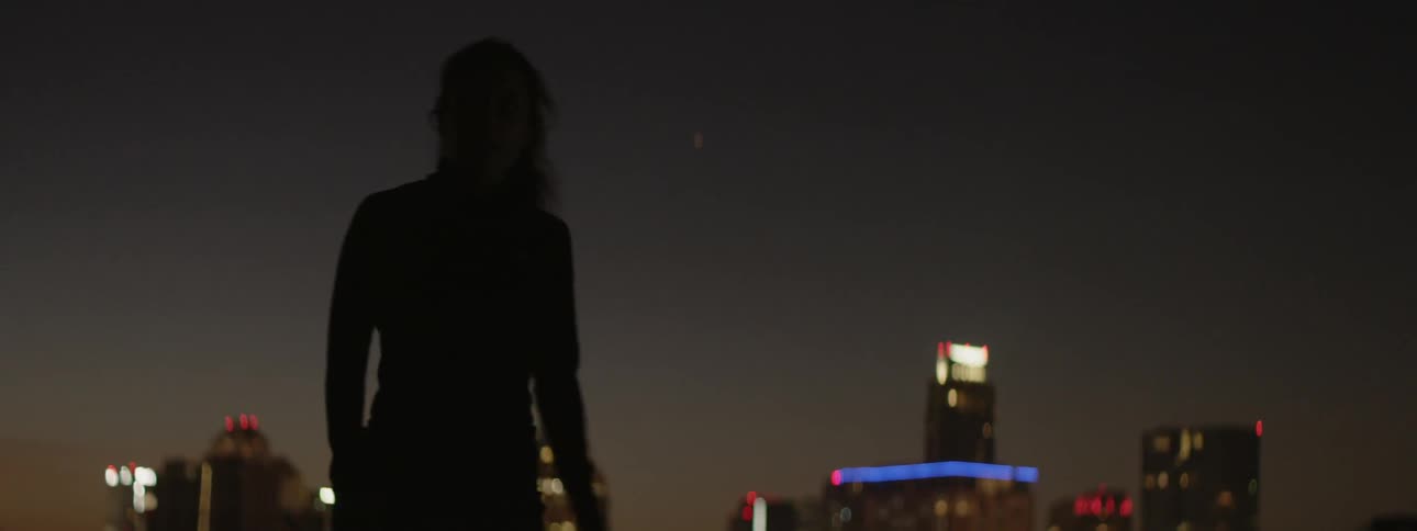 Woman stands in the shade by a city skyline at night