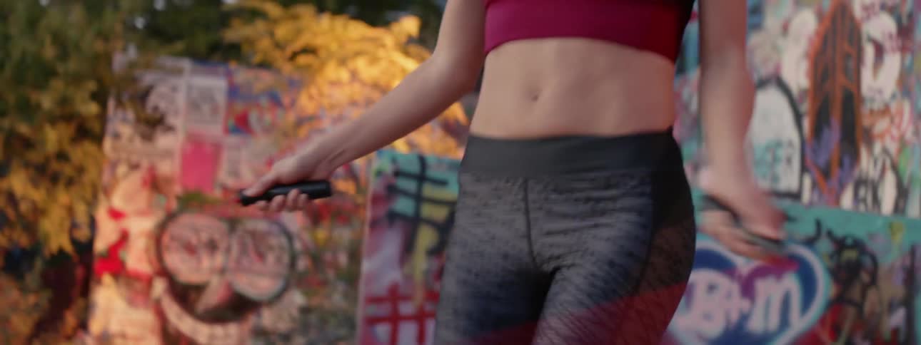A woman jumps rope outside in front of a graffiti covered wall