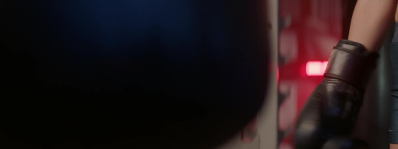 A woman wears boxing gloves next to a punching bag