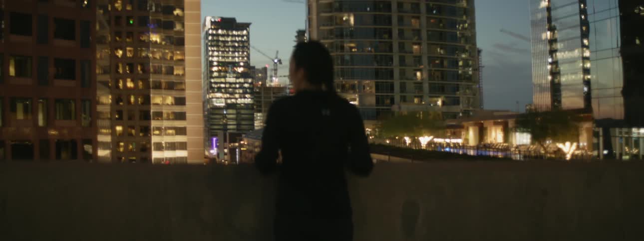 Woman standing and leaning on a short wall of a rooftop and looking at the city around her