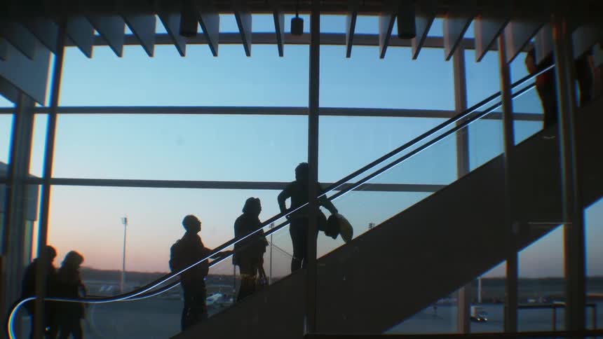 People using an escalator to go up to another floor in an airport at sunset