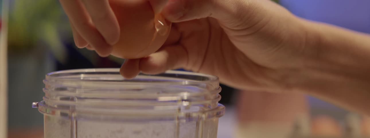 A woman adds an egg into a glass container
