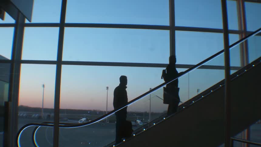 People are going up an escalator at an airport at dusk