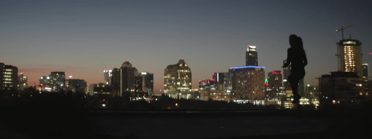 A female athlete is training on the outskirts of a city at dusk