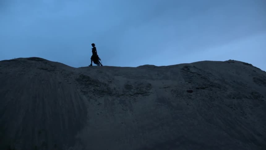 A woman wearing a dress is walking along a ridge line at dusk in the desert
