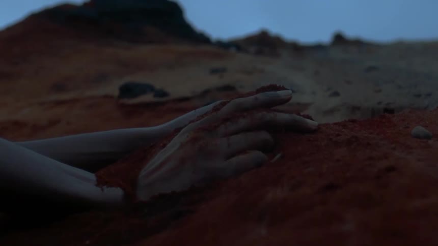 A person runs their hands through the dirt in a desert