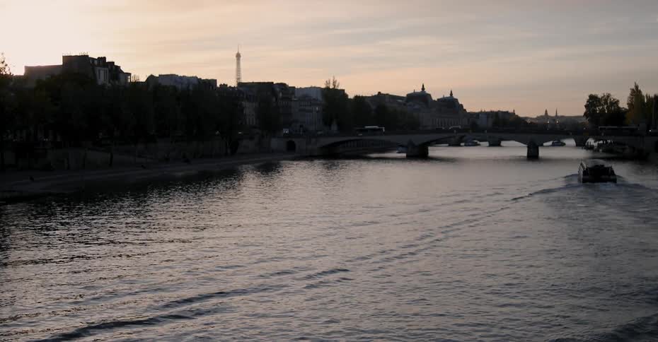 A boat floats on a city river at sunset