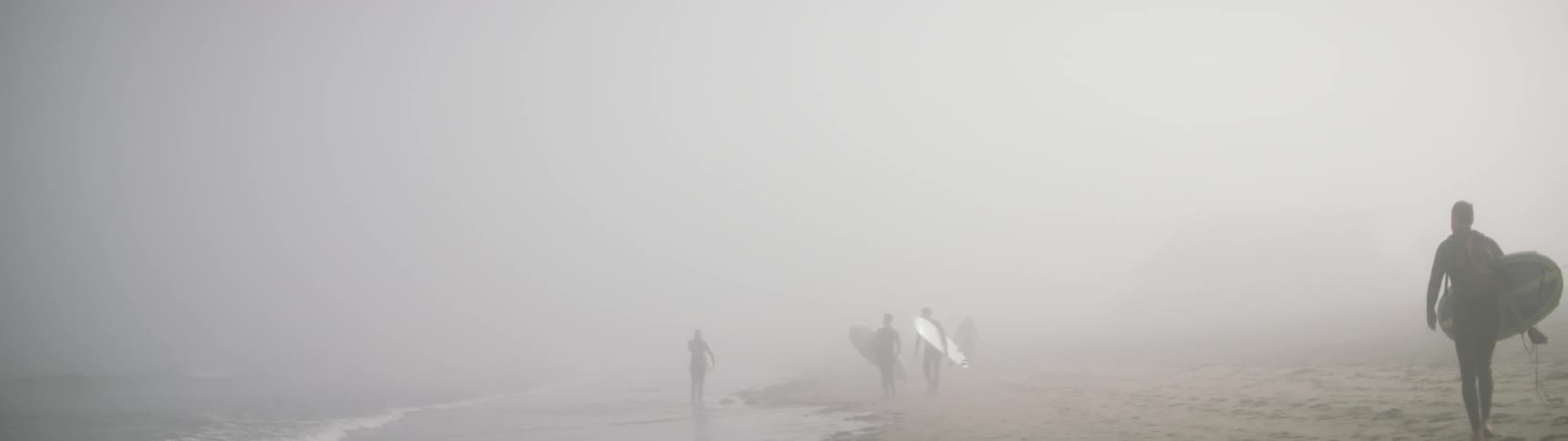 Three surfers walk on the beach