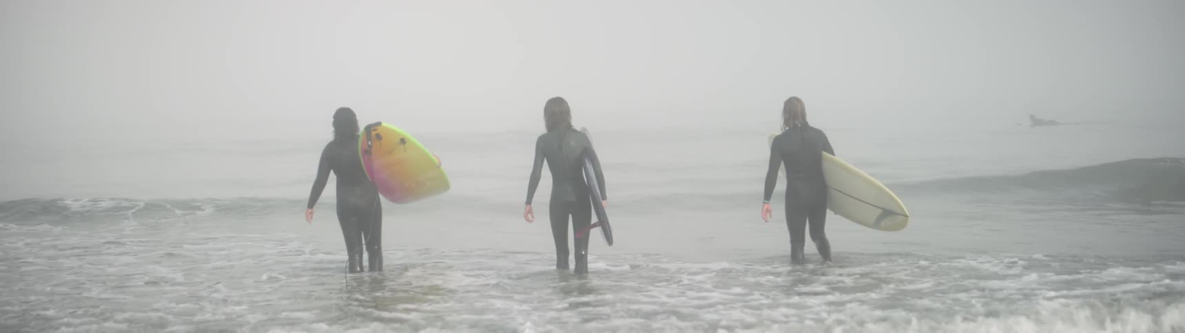 The people carry their surfboards into the foggy surf