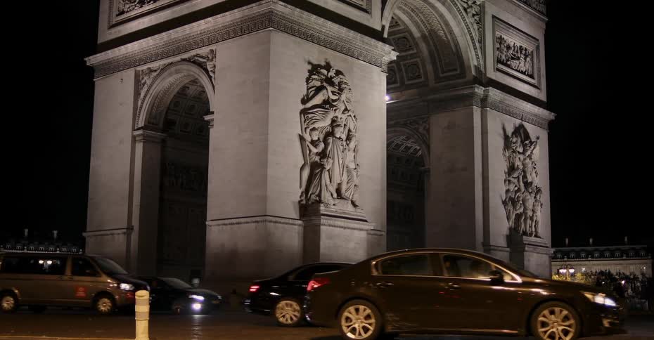 Vehicles are passing by the arc de triomphe at night