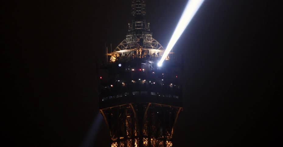 A spotlight shines from atop a tall building