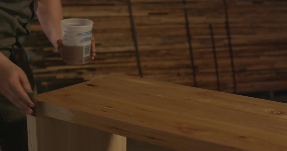 A person cleans a wood bench inside a workshop