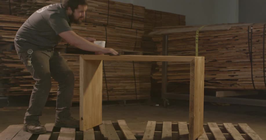 A worker at a furniture factory rubs polish on a piece of wooden furniture