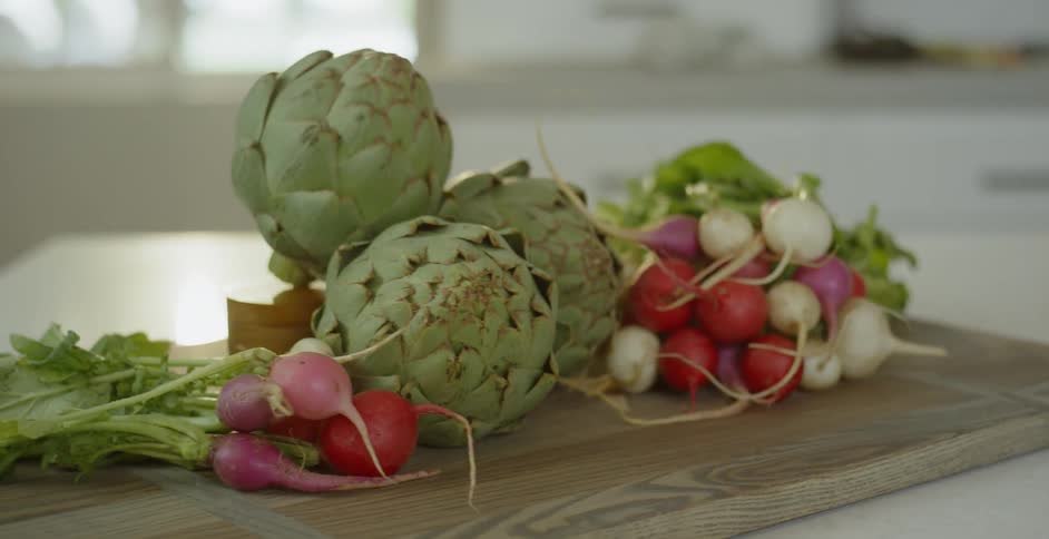 Artichokes and radishes sit on a cutting board