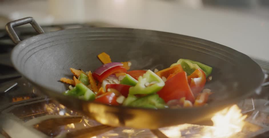 A woman cooks a stir fry of vegetables in a wok