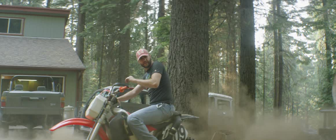 Motorcyclist spinning out and kicking up dirt next to another rider in the forest