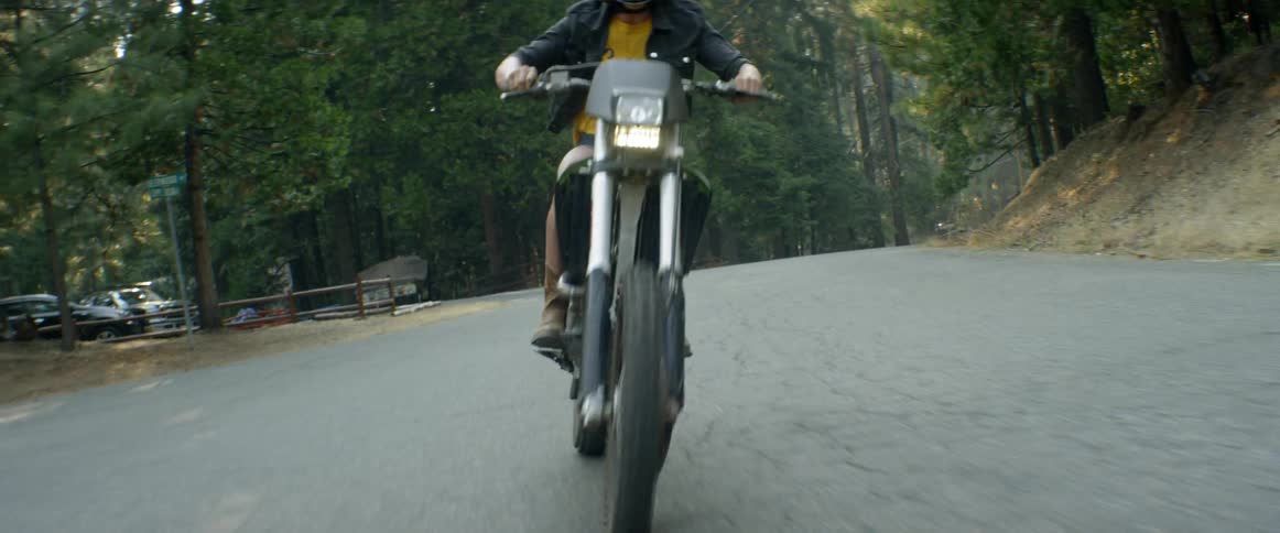 A woman is doing a wheelie as she rides a motorcycle in a natural setting during the day
