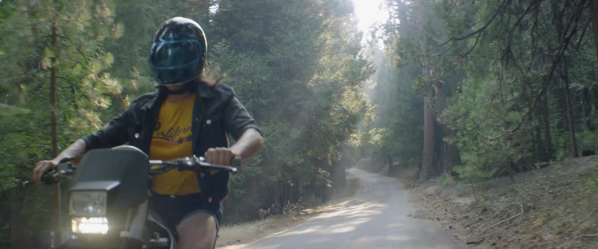 A woman performs a wheelie with a dirt bike on a forest road