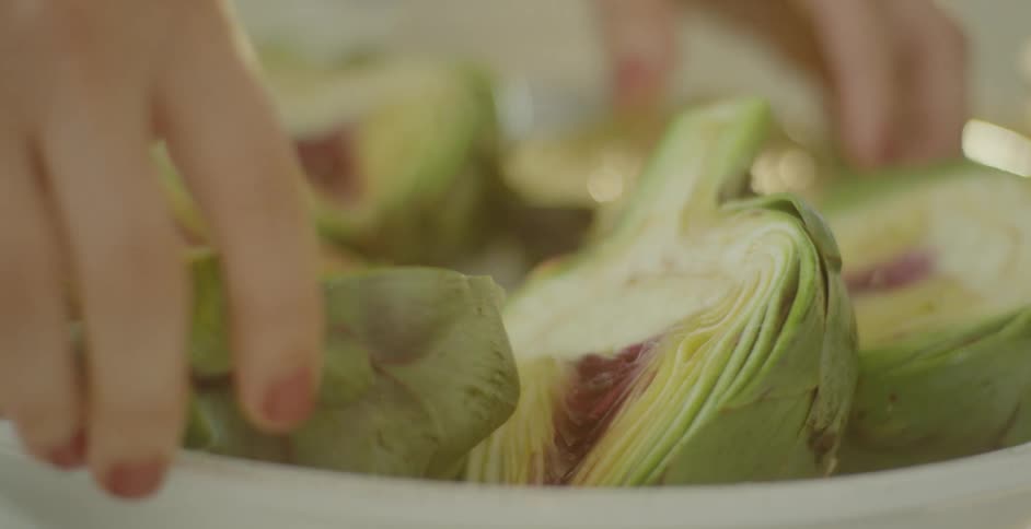 A woman is placing artichoke halves into a bowl in a kitchen in daylight