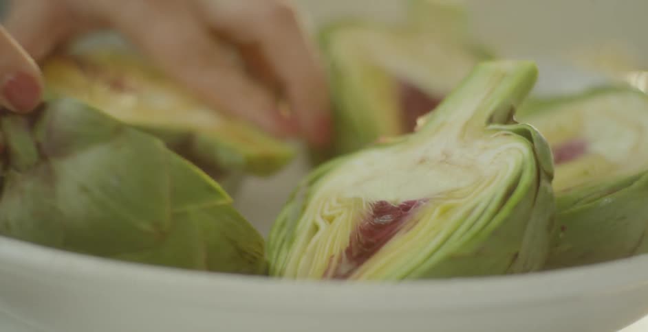 A person is lifting artichoke pieces in the bowl