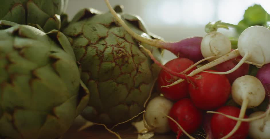 A bunch of red and white radishes and several artichokes