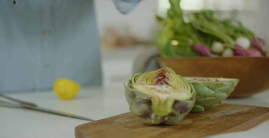 A woman is squeezing lemon over an artichoke in a kitchen during the day