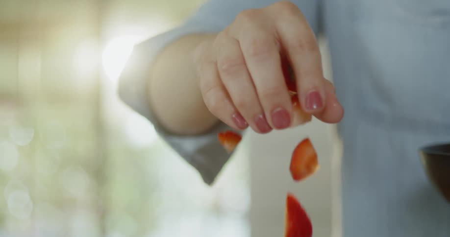 A woman makes a salad in a wood bowl with strawberries