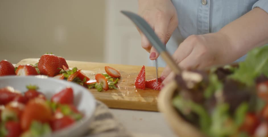 A woman is slicing strawberries in a kitchen in daylight