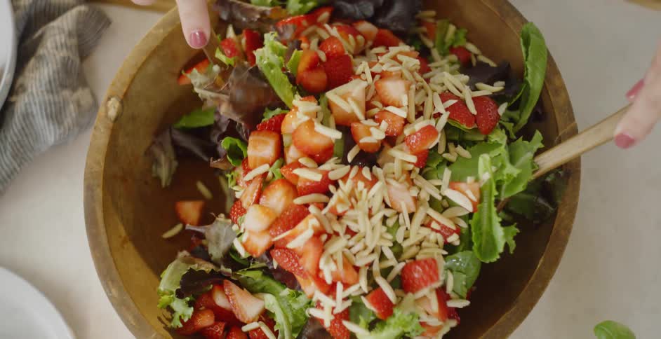 A woman mixes a salad in a wooden bowl