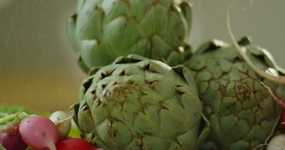 Liquid is sprinkled on radishes and artichokes on a cutting board
