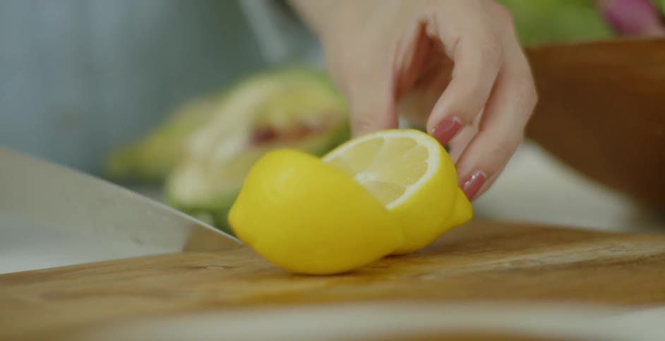 A woman slices a lemon on a wood cutting board