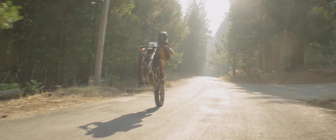 A woman is doing a wheelie as she rides a motorcycle in a natural setting during the day