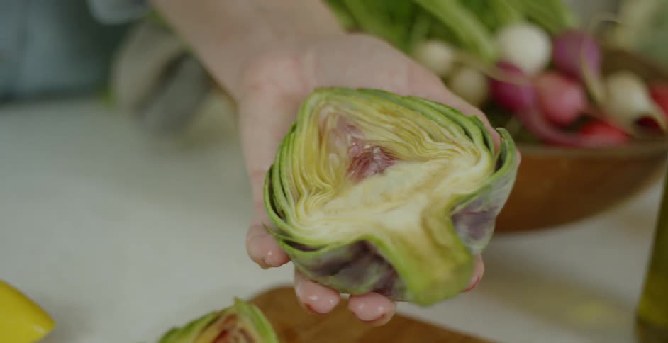 A woman is drizzling lemon onto an artichoke half she is holding