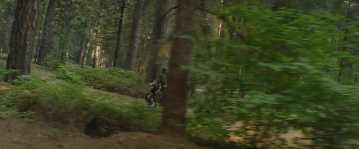 A woman is riding a motorcycle on a dirt trail through a forest in daylight