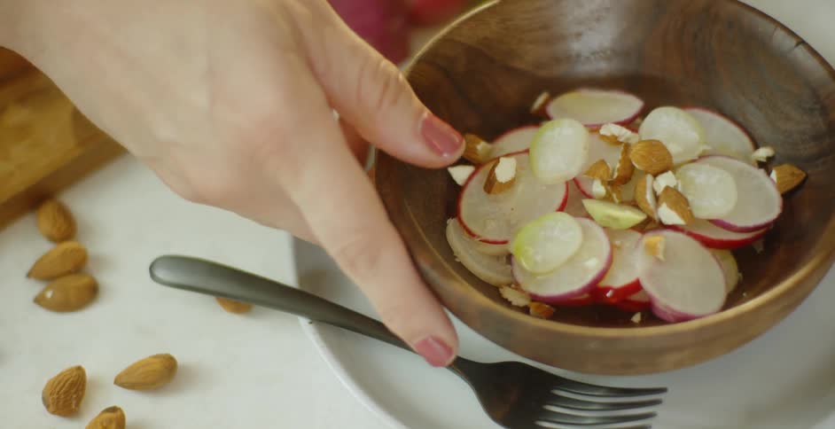 A woman grabs a bowl of sliced vegetables and nuts