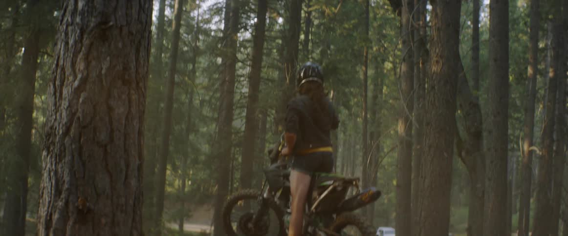 A woman stands up on a motorcycle on a dirt hill